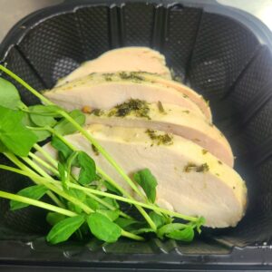Sliced chicken breast with herb seasoning and arugula greens in a dark skillet pit center stage.